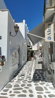 an alley way with white buildings and gray polka dots on the pavement, under a blue sky