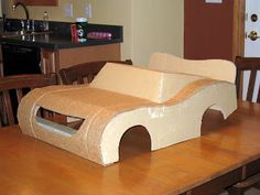 a cardboard car sitting on top of a wooden table in front of a kitchen counter