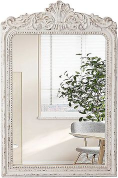 an ornate white framed mirror in front of a table with a potted plant on it