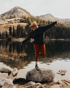 a woman standing on top of a rock next to a lake