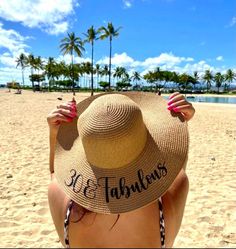 a woman wearing a hat on the beach with her name written on it and palm trees in the background