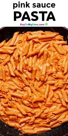 a pan filled with pink sauce pasta on top of a wooden table next to a green sign