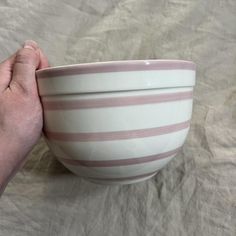 a hand is holding a striped bowl on top of a tableclothed surface with white and pink stripes