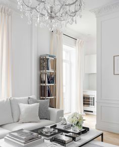 a living room filled with white furniture and a chandelier hanging from the ceiling