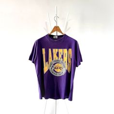 90s Los Angeles Lakers NBA t-shirt/ L * PLEASE READ BEFORE PURCHASE * PLEASE consider the PHOTOS before making the decision * The images may DIFFER in appearance from the actual product because we took pictures under daylight.  * PLEASE send your PHONE NUMBER after your purchase for the shipping company to contact you X No returns X No refund Condition : 9/10 More details : look at the pictures  Brand : Trench Size : L Pit to pit/ Chests : 20.5/41 inches  Length : 27.5 inches  Material : cotton   Color : purple  * ALL ITEMS are VINTAGE which may show some signs of wear and tear * Due to the different display and different light, the picture may not reflect the actual color of the item * Please, remember that our items are vintage so they may show some signs of wear, tear and yellow stains. Throwback Basketball Crew Neck T-shirt, Throwback Basketball T-shirt With Crew Neck, Throwback Basketball T-shirt With Short Sleeves, 90s Purple T-shirt With Letter Print, 90s Style Purple T-shirt With Letter Print, Purple 90s Style T-shirt With Letter Print, 90s Style Screen Print T-shirt For Sports Events, Vintage Purple T-shirt With Letter Print, 90s Los Angeles