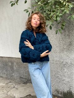 a woman standing in front of a tree wearing blue jeans and a fuzzy jacket with her arms crossed