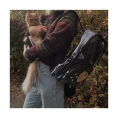 a person holding a cat in their arms and a backpack on his back with leaves around them