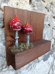 two red mushrooms sitting on top of a wooden shelf next to a stone wall with moss