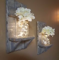 two mason jars with flowers are hanging on the wall