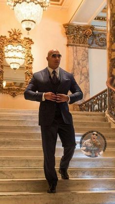 a man in a suit and tie walking down some stairs with chandeliers on either side