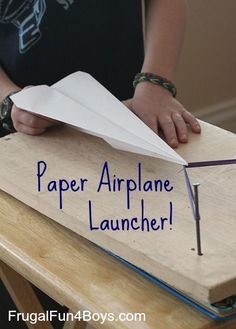 a person holding a paper airplane on top of a wooden board with the words paper airplane launcher written on it