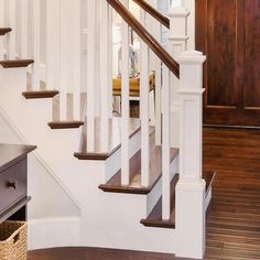 a white staircase with wooden handrails and wood flooring next to a brown door