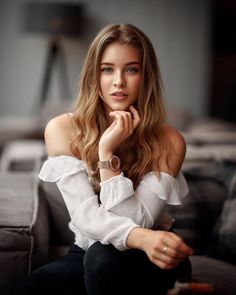 a woman sitting on top of a couch wearing a white shirt and black pants with her hand under her chin