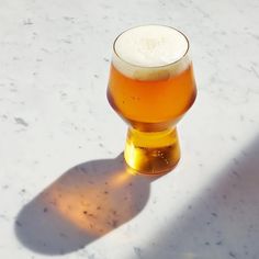 a glass of beer sitting on top of a white counter next to a light shadow