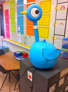 a blue bird sitting on top of a black box in front of a bulletin board