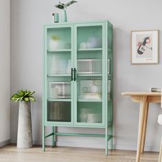 a green cabinet sitting next to a table with a potted plant on top of it