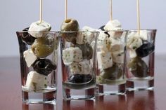 four glasses filled with olives, cheese and crackers sitting on top of a wooden table