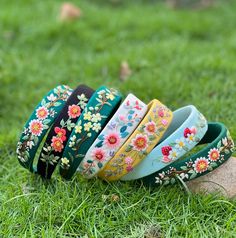 five different colored bracelets sitting on top of a rock in the grass with flowers painted on them