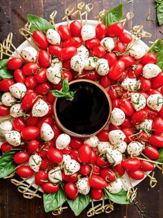 a platter filled with tomatoes and mozzarella on skewers, garnished with basil leaves