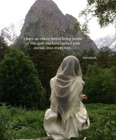 a woman sitting on top of a wooden bench covered in a white shawl next to mountains