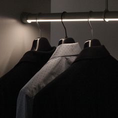 two shirts are hanging on a rail in front of a wall with a light behind them