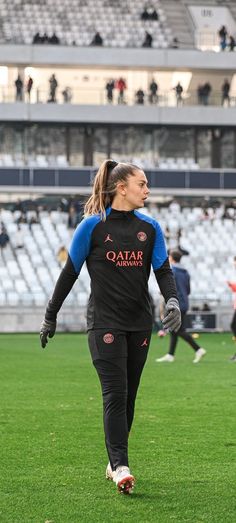 a woman in black and blue uniform running on field with soccer ball near her feet