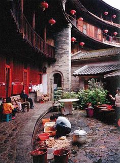 people are sitting in the courtyard of an old chinese building with red lanterns hanging from it's roof