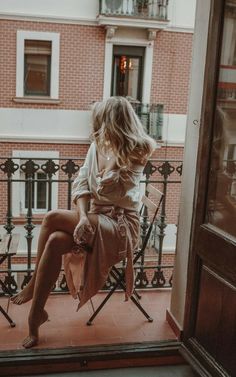 a woman sitting on top of a chair in front of a window next to a balcony