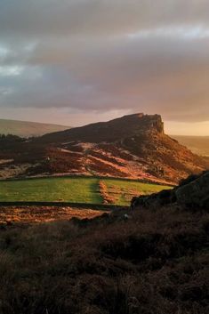 the sun is setting on a hill with grass and hills in the foreground behind it