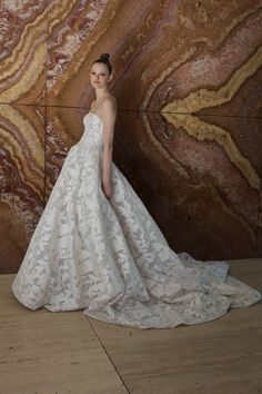 a woman standing in front of a marble wall wearing a white wedding dress with an open back