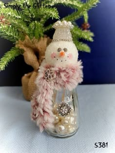 a small snowman in a glass jar with pearls and a bow on the neck