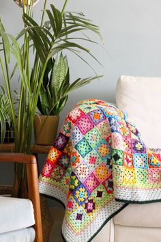 a crocheted blanket is sitting on a couch next to a potted plant