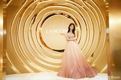 a woman standing in front of a gold and white wall with the word lanco on it