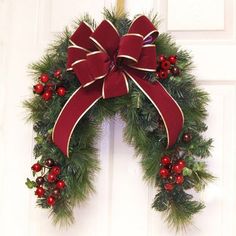 a christmas wreath hanging on the front door with red berries and evergreens around it