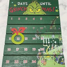 a green wooden calendar with the grinch on it's face and numbers for each month