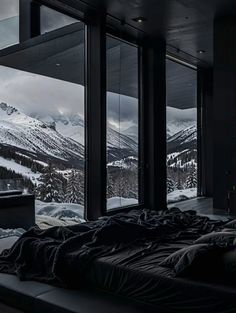 a bed sitting in front of a window next to a snow covered mountain side forest