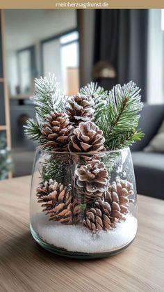 some pine cones and snow in a glass vase on a table with the words christmas decorations