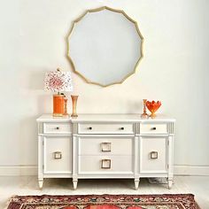 a white dresser with two drawers and a round mirror above it on top of a rug