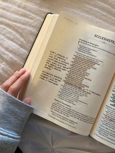 someone is reading a book on the bed with their hand resting on the open book