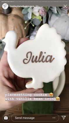 someone holding up a cookie with the word julia on it in front of some flowers