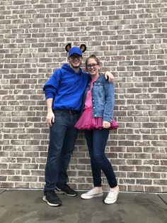 a man and woman standing next to each other in front of a brick wall wearing mickey ears