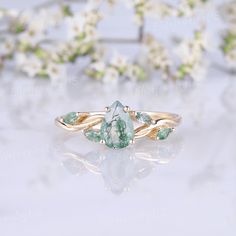 an image of a ring with green stones on it and white flowers in the background