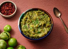 there is a bowl of green food next to some other foods on the table with spoons