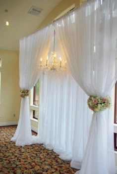 a room with white drapes and chandelier hanging from it's ceiling