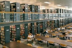 people are sitting at tables and reading books in a library with many shelves full of books