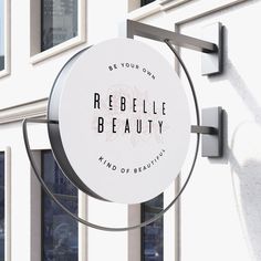 a round sign hanging from the side of a building that says, be your own rebelle beauty