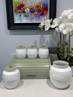 white vases sitting on top of a counter in front of a painting and flowers