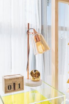 a glass table topped with a lamp next to a wooden box and window sill