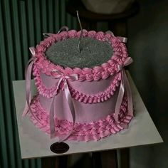 there is a pink cake that has been decorated with ribbons