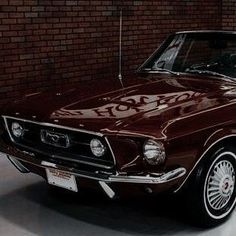 an old ford mustang parked in front of a brick wall